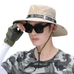 Chapeau solaire beige anti-UV et imperméable à bord large, porté par un homme en tenue camouflée avec lunettes de soleil.