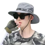 Jeune homme portant un chapeau solaire imperméable anti-UV à larges bords, associé à un t-shirt camouflage et des lunettes de soleil.
