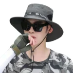 Chapeau solaire imperméable anti-UV à large bord, idéal contre soleil et pluie, porté avec lunettes, gilet camouflé et gants.