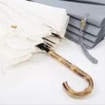 Grand parapluie canne en bambou avec toile blanche, design élégant, accompagné de parapluies gris pliés en arrière-plan.
