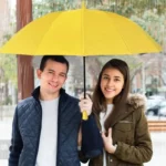 Un couple souriant sous un grand parapluie jaune robuste, parfait pour l'hiver en ville, issu de notre collection [Collection].
