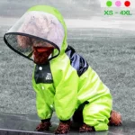Chien portant une combinaison imperméable intégrale verte avec capuche et visière transparente, idéal pour la pluie.