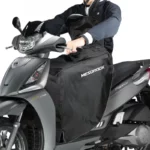 Conducteur de scooter équipé d'une jupe et tablier coupe-vent imperméable, idéal pour protection contre la pluie en circulation.