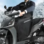 Conducteur en scooter équipé d'une jupe et tablier coupe-vent noir, protection idéale pour l'hiver sur fond enneigé.