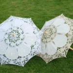 Parapluie enfant en dentelle blanche 60 cm, élégant et stylé, parfait pour mariages, posé sur une pelouse verte avec motifs floraux.
