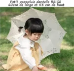 Parapluie enfant en dentelle 60 cm, beige, idéal pour mariage, petite fille assise dans l'herbe, élégance et protection solaire.