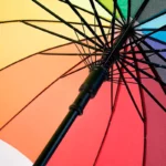 Parapluie femme multicolore avec motifs arc-en-ciel, structure noire robuste, idéal pour illuminer les jours de pluie.
