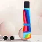 Mini parapluie multicolore automatique anti-UV, design moderne, plié avec lunettes de soleil sur fond pastel, pratique & élégant.