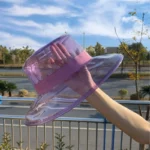 Chapeau de pluie transparent en borsalino avec bandeau rose, mode pratique et chic, parfait sous un ciel ensoleillé.