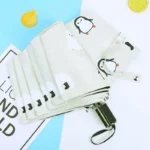 Parapluie beige pliable automatique avec motifs pingouins et ours polaires, design original, pratique et stylé contre la pluie.