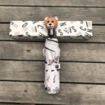 Parapluie beige luxe automatique avec poignée tête d'ours, élégant et pratique, présenté avec emballage sur fond en bois.