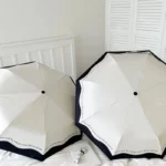 Parapluie blanc à bord noir anti-UV, élégant et pratique, parfait pour se protéger avec style. Accessoire chic et tendance.