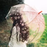 Femme avec parapluie transparent fleuri roses dans un champ verdoyant sous la pluie, accessoire tendance [Collection]