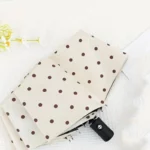 Parapluie ouvert blanc noir à pois blancs anti UV, posé élégamment avec fleurs, style chic et pratique pour toutes les saisons