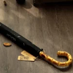 Parapluie canne élégant avec poignée en bambou, posé sur un sol en bois, style raffiné et protection idéale contre la pluie.