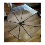 Parapluie transparent élégant, robuste et chic de la collection [Collection], ouvert sur un sol en bois, avec des rayons noirs visibles.