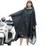 Femme avec poncho de pluie noir ample à capuche, design mode et pratique, idéale pour la pluie, posant près d'un scooter.