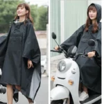Poncho femme noir avec capuche, élégant et pratique, idéal pour la pluie et la mobilité, ici porté par une femme souriante en scooter.