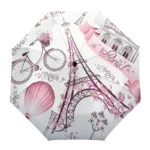 Parapluie élégant avec motifs de la Tour Eiffel, vélo, ballon, fleurs, tons rose et blanc, parfait pour un style parisien chic.