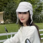 Jeune femme souriante avec bonnet blanc, pull en tricot, accessoires hiver molletonnés, protection pluie et neige en nature.