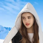 Femme en veste d'hiver avec capuche molletonnée et nœud, idéale pour la pluie et la neige, dans un paysage enneigé.