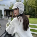 Capuche hiver molletonnée gris unisexe, cache-oreilles, femme souriante, moto, pull blanc, environnement extérieur verdoyant.