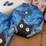Parapluie bleu foncé automatique avec motifs de chat noir, nuages bleus et étoiles brillantes, posé sur une moquette élégante.