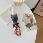 Parapluie beige automatique à motif de tête de chat noir et fleurs, décoré sur une table avec magazines et illustrations colorées.