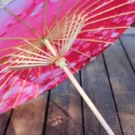 Parapluie chinois rouge en papier huilé avec motifs floraux, accessoire élégant et décoratif, posé sur un sol en bois.