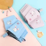Parapluies lapin pour enfant anti-UV, motifs colorés coeurs et lapins, disponibles en bleu et rose sur fond pastel.
