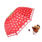 Parapluie manuel rouge à motif fraise avec gouttes blanches, élégant et pratique, idéal sous la pluie, panier fleuri en décor.