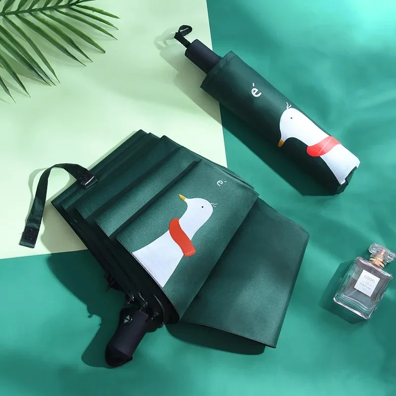 Parapluie pliable vert motif canard écharpe, design original et automatique, posé sur fond vert avec parfum élégant.