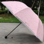 Parapluie rose pliant manuel avec dentelle froufrou, design floral élégant, parfait pour allier protection et raffinement.