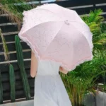 Parapluie rose pliant en dentelle pour mariage, élégant accessoire féminin, cadre tropical avec cactus en arrière-plan.