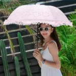 Parapluie rose pliant manuel à dentelle froufrou, élégant accessoire féminin, idéal pour soleil ou pluie, ambiance nature et chic.