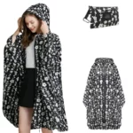 Poncho femme noir motifs floraux blancs avec capuche, fermeture éclair, élégant et pratique, accompagné d’un étui assorti.