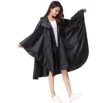 Femme souriante en poncho long noir zippé, manches amples, sous la pluie, alliant élégance et praticité pour toutes les tailles.