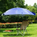 Parapluie de pêche léger bleu, déployé dans un jardin, offrant une protection solaire près d'une chaise pliante et d'une table.
