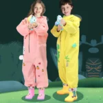Enfants portant des ponchos imperméables 3D animaux rose et jaune, jouant joyeusement avec des pistolets à eau dans une forêt stylisée.