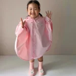 Petite fille joyeuse portant un poncho enfant motif ours et lapin, de la collection [Collection], avec bottes assorties.