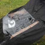 Poncho de pluie noir imperméable avec fenêtre transparente, adapté pour chariot motorisé, sur fond de pelouse fleurie.