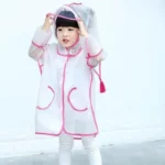 Enfant avec poncho imperméable transparent à boutons, détails roses, collection [Collection], idéal pour rester au sec sous la pluie.