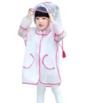 Enfant avec poncho imperméable transparent, bordures roses, boutons pression, ajustant sa capuche. Idéal pour la pluie.