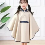 Poncho pluie fille beige avec capuche, enfant souriante dans une pièce lumineuse, tenue imperméable mode et pratique, collection [Collection].