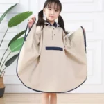 Poncho pluie fille beige avec capuche et manches larges, de la collection [Collection], imperméable de qualité devant un décor lumineux.