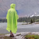 Poncho pluie homme jaune vif près d'un lac montagneux sous la pluie légère, idéal pour rester au sec en toutes conditions.