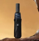 Parapluie automatique femme élégant noir avec bandes bleues, design moderne sur fond doré, idéal pour un style chic et pratique.