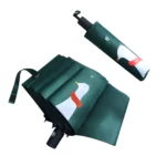 Parapluie pliable vert motif canard écharpe, design original et automatique, posé sur fond vert avec parfum élégant.