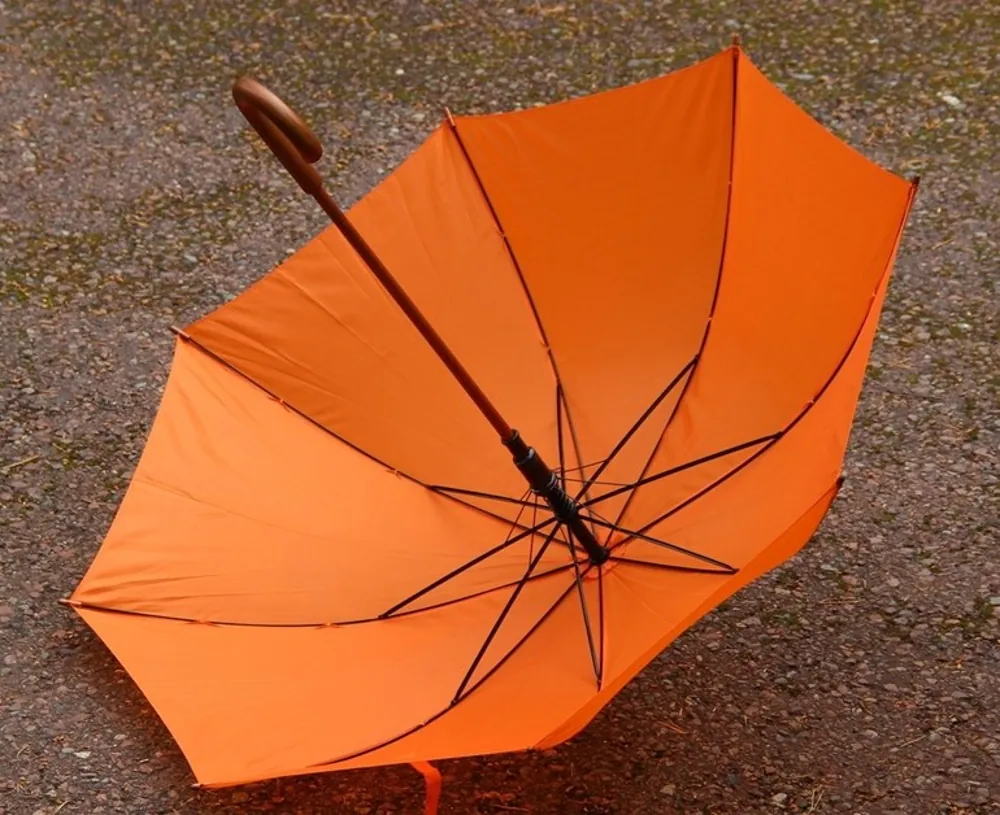 Parapluie orange ouvert au sol, robuste et raffiné. Tissu résistant et manche en bois, parfait pour affronter les averses avec élégance et originalité.