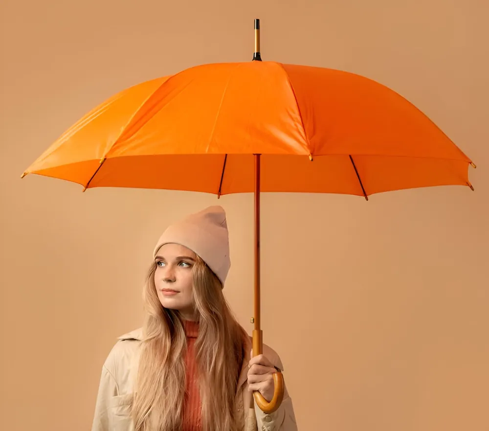 Femme au chapeau beige tenant un parapluie orange vif. Look moderne et lumineux pour un accessoire indispensable lors des journées pluvieuses.